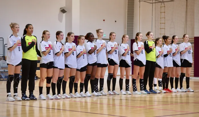 Eine Handball-Frauenmannschaft steht zusammen in einer Halle und lacht. 