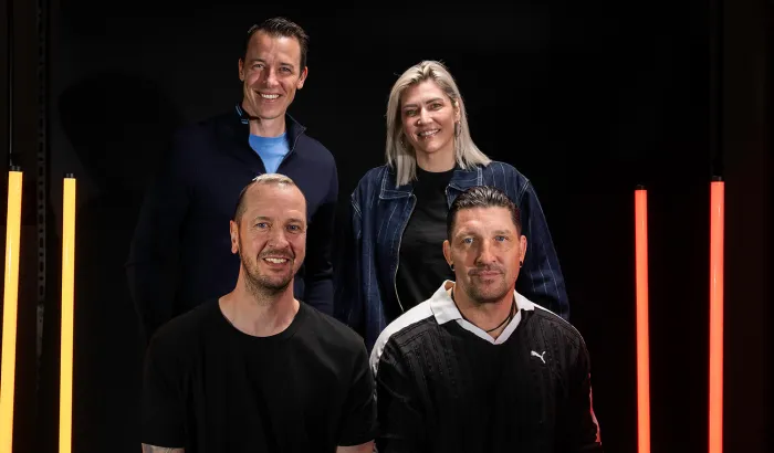 Die 4 WM-Botschafter gemeinsam beim Fotoshooting vor schwarzem Hintergrund mit gelben und roten Lichtsäulen.