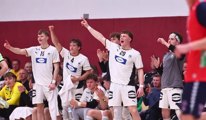 Eine Truppe von Handballern in weißen Trikots die jubeln und an der Auswechselbank stehen 