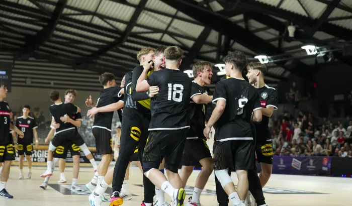 Eine Truppe von Handballerinnen in schwarzen Trikots die bei einem Tor aufstehen und jubeln