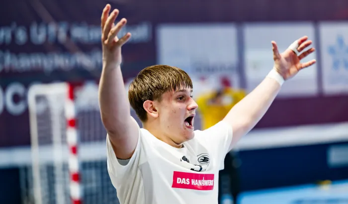 Ein junger Mann in einem weißen Trikot der die Hände in die Luft streckt und schreit. 