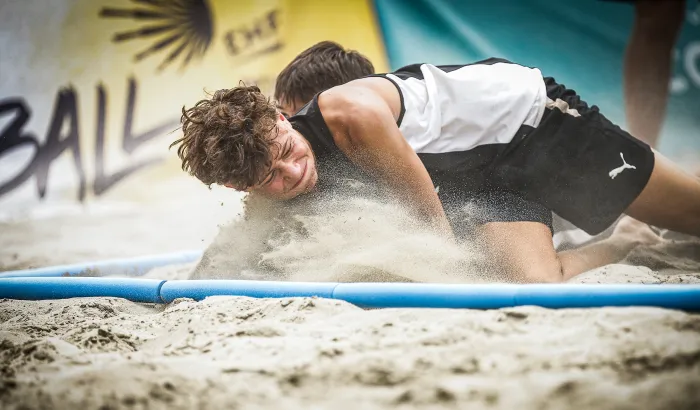Zwei Spieler kämpfen im Sand um den Ball.