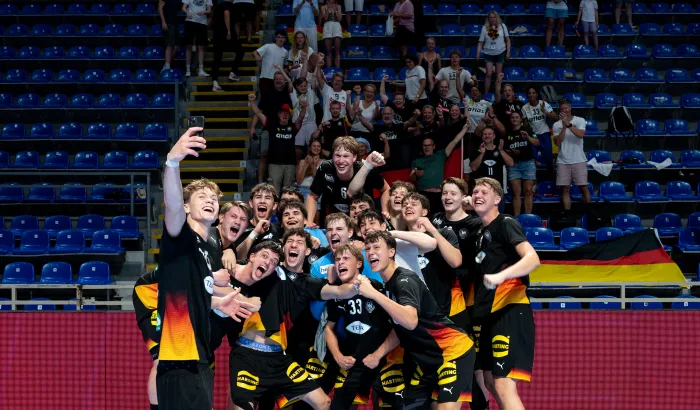 Eine Gruppe junger Männer in schwarzen Trikots die ein Selfie machen und in die Kamera Jubeln.
