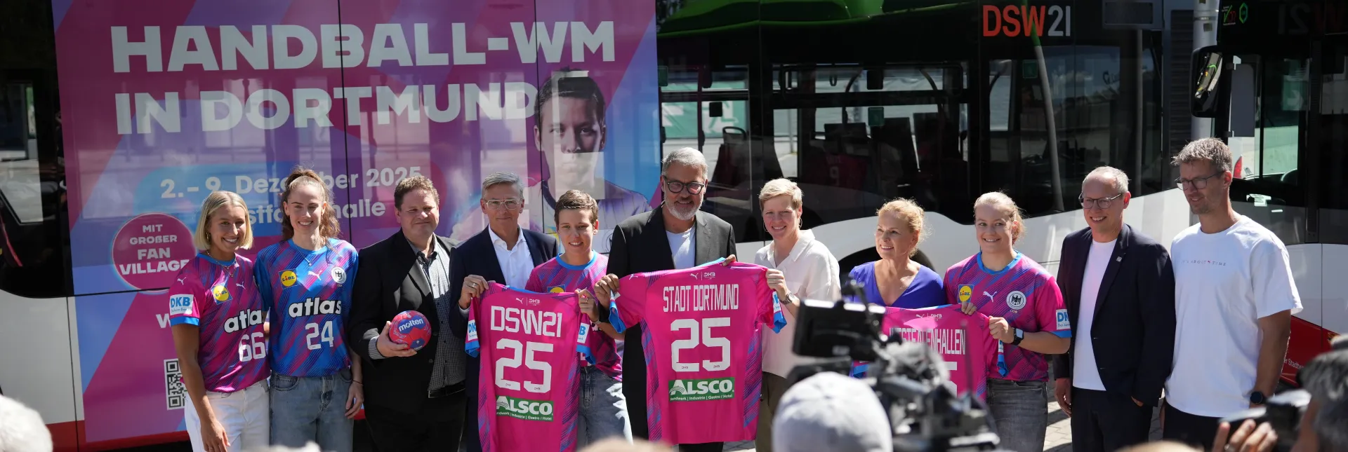Gruppe posiert vor Westfalenhalle mit Bus im Handball-WM 25 Branding