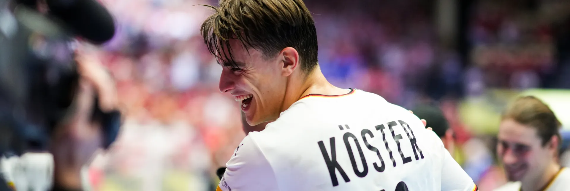 Ein junger Mann im Deutschland Trikot der lachend jemanden umarmt. 