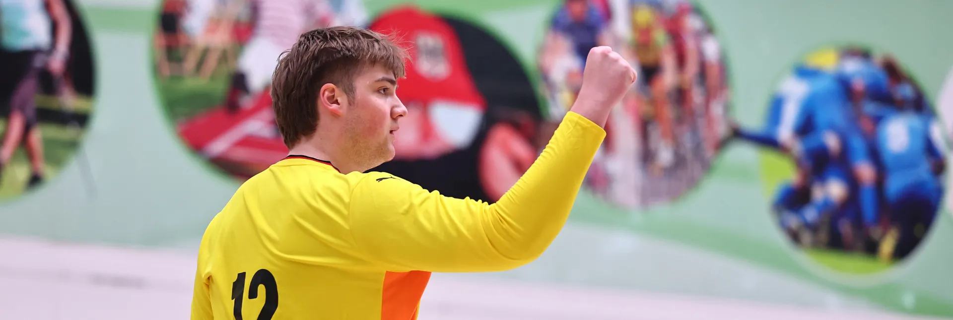 Ein junger Mann in einem orangen Trikot der die Faust ballt und sich freut. 