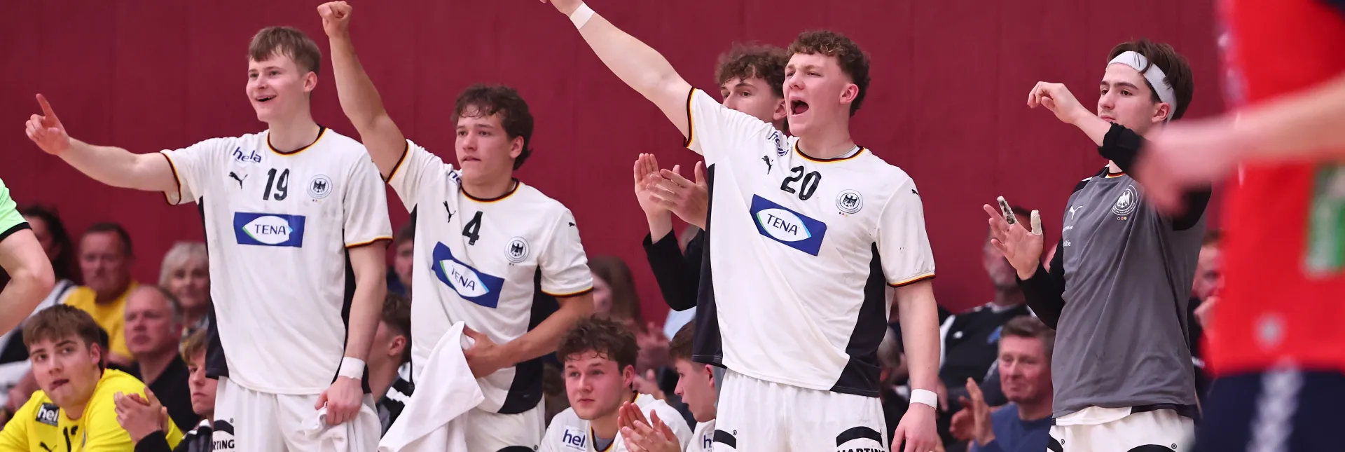Eine Truppe von Handballern in weißen Trikots die jubeln und an der Auswechselbank stehen 