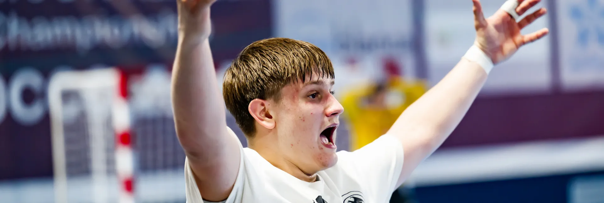 Ein junger Mann in einem weißen Trikot der die Hände in die Luft streckt und schreit. 