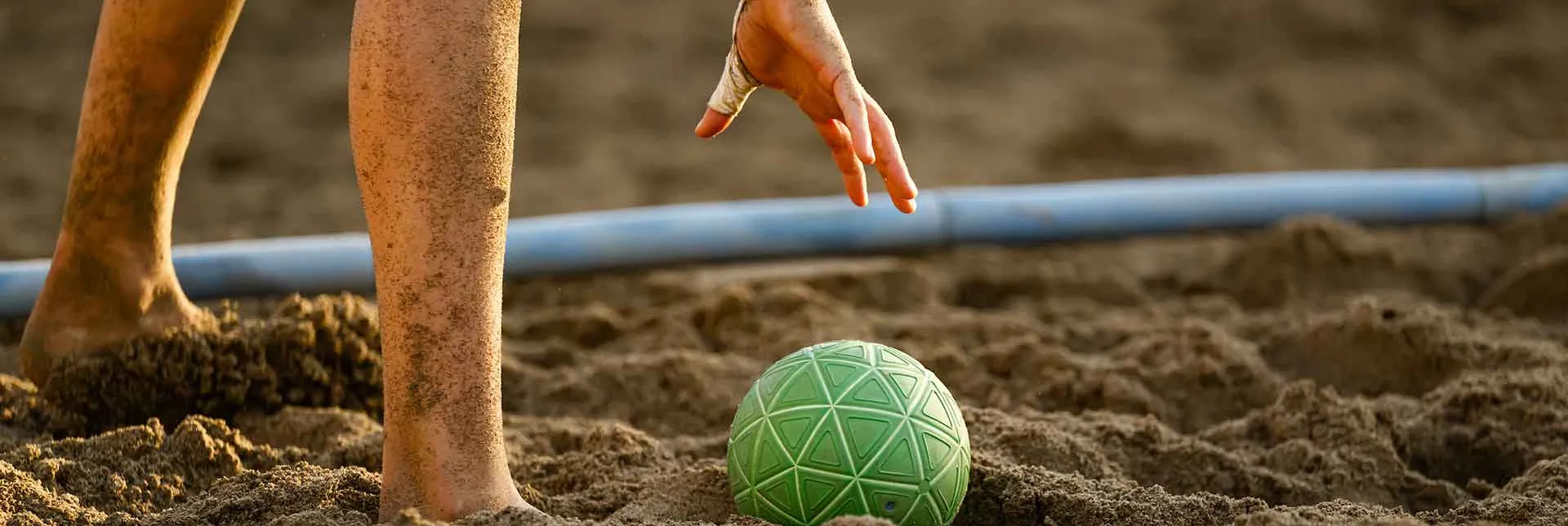 Eine Hand hebt den Beachhandball aus dem Sand