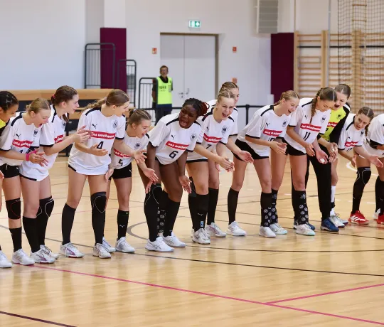 Eine Handball-Frauenmannschaft steht zusammen in einer Halle und lacht. 
