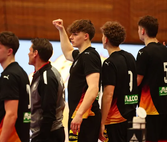 Eine Truppe Männer die in einer Handballhalle stehen und jubeln 