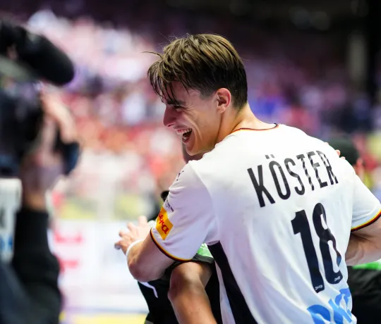 Ein junger Mann im Deutschland Trikot der lachend jemanden umarmt. 