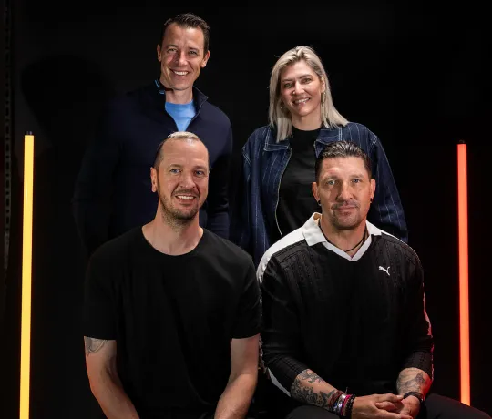 Die 4 WM-Botschafter gemeinsam beim Fotoshooting vor schwarzem Hintergrund mit gelben und roten Lichtsäulen.