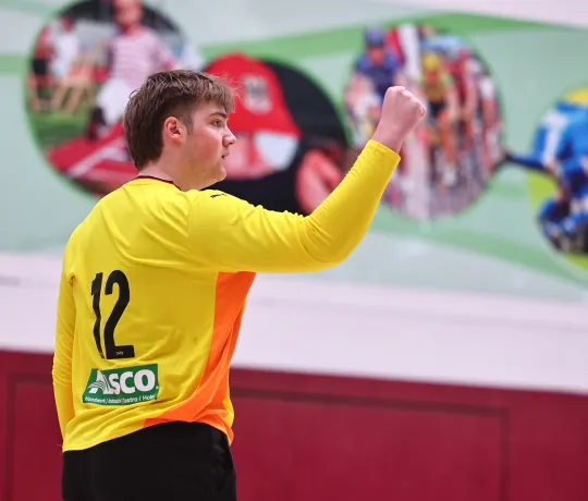 Ein junger Mann in einem orangen Trikot der die Faust ballt und sich freut. 