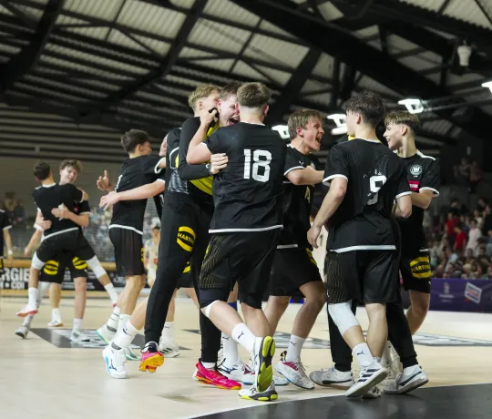 Eine Truppe von Handballerinnen in schwarzen Trikots die bei einem Tor aufstehen und jubeln