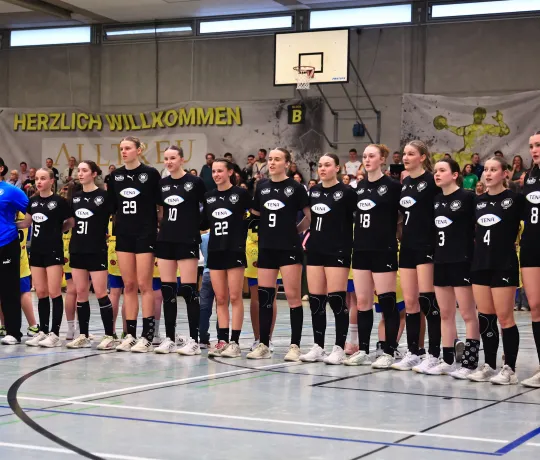 Eine Truppe von Mädels in Hnandballsachen, die zusammenstehen mit den armen ineinander verschlungen.. 