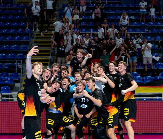 Eine Gruppe junger Männer in schwarzen Trikots die ein Selfie machen und in die Kamera Jubeln.