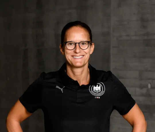 Eine Frau in einem schwarzen Shirt die lacht und die Arme seitlich aufgestellt hat. 