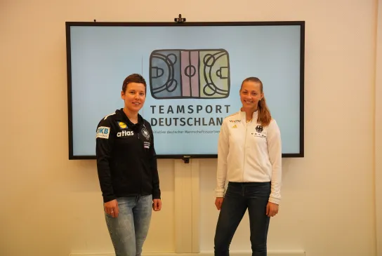 Zwei Spielerinnen vor einem großen Screen stehend.