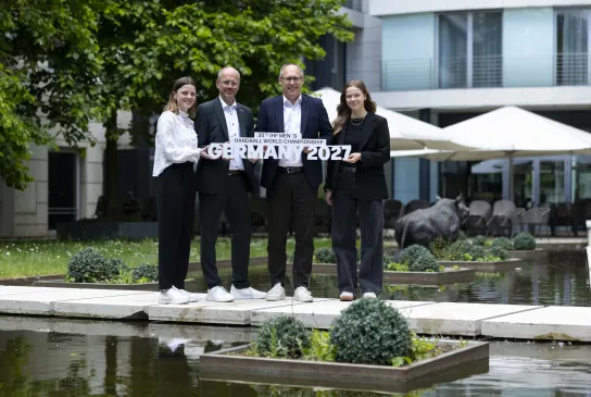 Zwei Männer und zwei Frauen halten vor einem Radisson Hotel den Schriftzug der Handball-Weltmeisterschaft 2027 in die Höhe.