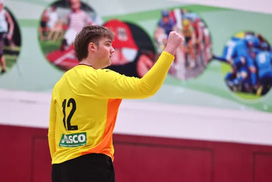 Ein junger Mann in einem orangen Trikot der die Faust ballt und sich freut. 
