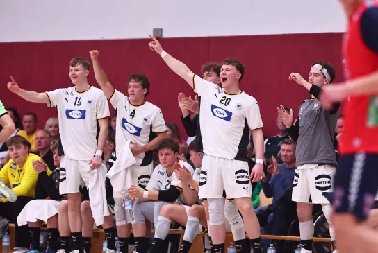 Eine Truppe von Handballern in weißen Trikots die jubeln und an der Auswechselbank stehen 