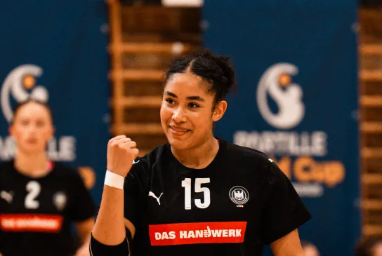 Eine junge Frau in einem schwarzen Trikot, die die Faust reckt und sich freut.