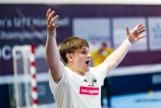 Ein junger Mann in einem weißen Trikot der die Hände in die Luft streckt und schreit. 