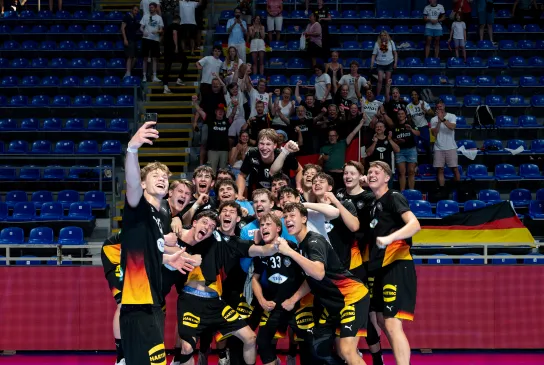 Eine Gruppe junger Männer in schwarzen Trikots die ein Selfie machen und in die Kamera Jubeln.