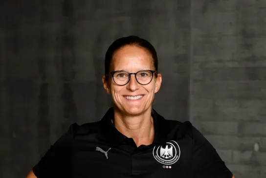 Eine Frau in einem schwarzen Shirt die lacht und die Arme seitlich aufgestellt hat. 