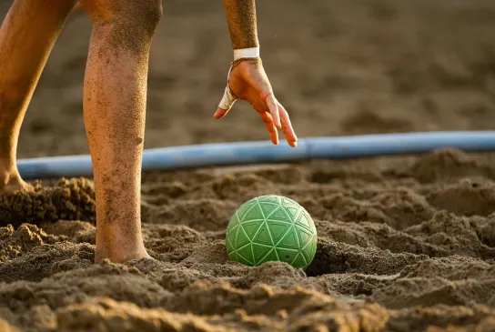 Eine Hand hebt den Beachhandball aus dem Sand